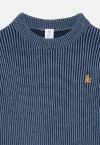 Maglione lavorato a maglia in blu navy scuro con strisce azzurro chiaro. Presenta un collo a coste e una piccola ricamatura di un orso marrone chiaro sul petto.