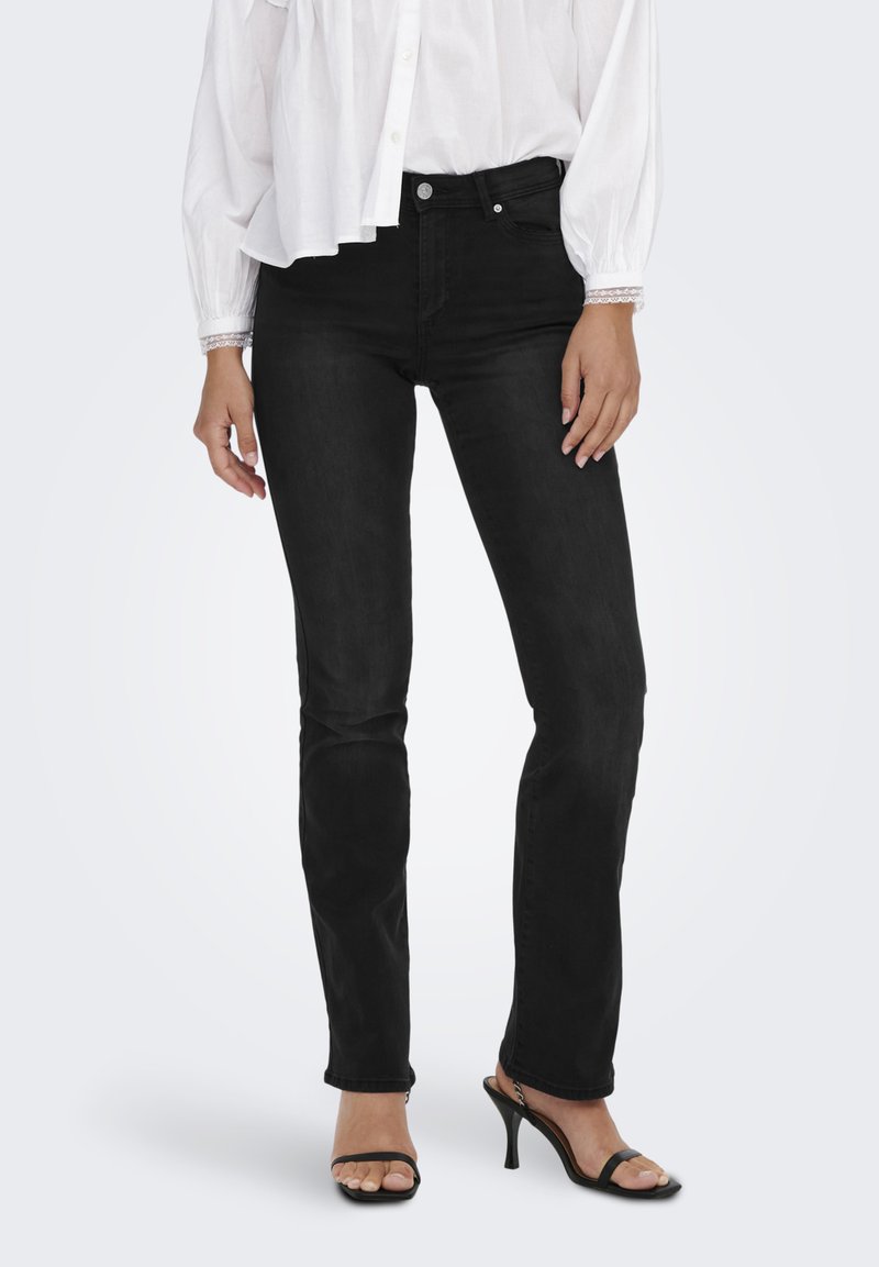 Svarte denimjeans med en tettsittende design, fem lommer og lett stretch. Kombinert med en løs hvit skjorte og høyhælede sandaler.