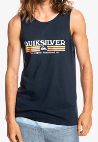 Marinblå linne i bomull med en tydlig "Quiksilver" logotyp och randiga detaljer i orange och gult. Har en rundad halsringning.