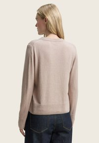 Pull en maille rose clair à col rond, avec des poignets et un ourlet côtelés. Présente une coupe décontractée et des coutures minimales, associé à un jean en denim sombre.