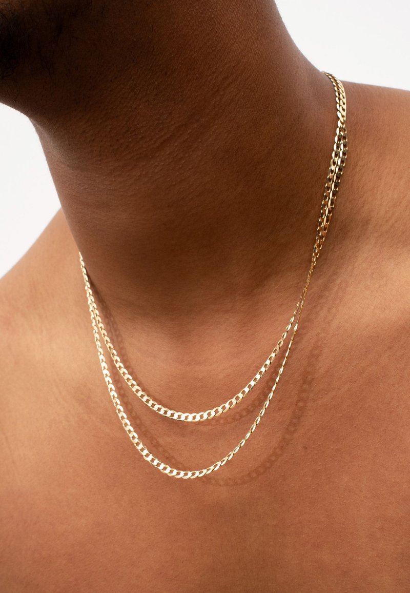 Goldene Kettenhalskette mit drei Schichten flacher Glieder, glänzender Oberfläche und glatter Textur auf nacktem Hals.