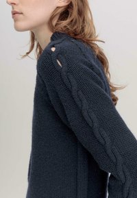Gewebter marineblauer Pullover mit strukturiertem Muster, der geflochtene Akzente an den Ärmeln und Schlitze in der Nähe der Schultern aufweist.
