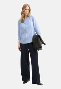 Light blue, collared shirt with three-quarter sleeves and two chest pockets, paired with dark wide-leg trousers and a black leather bag.