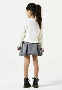 Witte gebreide trui met gestructureerde mouwen, gecombineerd met een grijze denim rok. Zwarte enkelboots met gele accenten en veters.