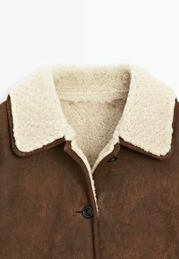 Bruine nepleer jacket met een crèmekleurige sherpa kraag, voorzien van zwarte knopen en een zachte, gestructureerde binnenvoering.