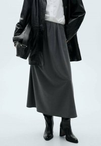 Grauer, mittellanger Rock aus weichem Stoff, kombiniert mit einem weißen Hemd und einer schwarzen Lederjacke. Schwarze Stiefel mit Absatz und eine passende Handtasche runden das Outfit ab.