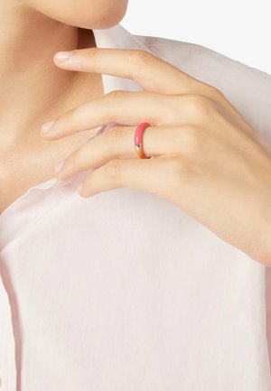 Hand with pale skin wearing a red and orange enamel ring on the middle finger, resting near the neck and white shirt collar.