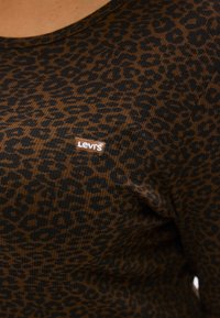 Ruda šviesų tekstūros marškinėliai su juodais leopardų raštais, viršutinėje kairėje pusėje yra mažytė balta Levi's logotipo žymė.