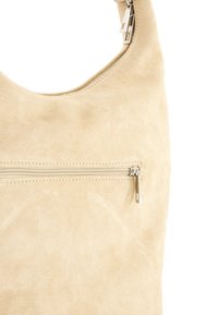 Beige Wildleder Schultertasche mit glatter Textur, ausgestattet mit einer vorderen Reißverschlusstasche und silbernen Hardware-Akzenten. Abgerundete obere Öffnung.