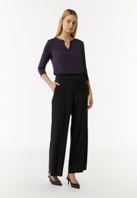 Dunkelviolette, leichtgewichtige Bluse mit einem Spitzenausschnitt, kombiniert mit hochgeschnittenen, schwarzen, weiten Hosen; beide zeichnen sich durch eine glatte Textur aus.