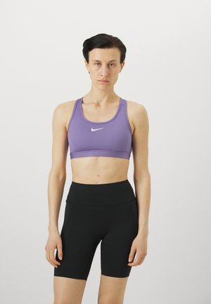 Lilla idretts-BH med racerback-design og hvit logo, kombinert med høyt midje svarte shorts med en glatt tekstur og tettsittende snitt.