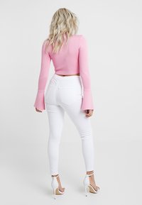 Růžový krátký svetr s rozšířenými rukávy ve spojení s bílými slim džínami a bílé sandály na vysokém podpatku se šněrováním. Hladká textilie.