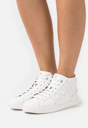 Witte hoge sneakers met geperforeerd "JOOP!"-logo en gouden veteroogjes, gedragen op blote benen tegen een effen witte achtergrond.