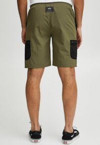 Olivenfarvede shorts lavet af letvægtsmateriale har en sort mesh-lomme på højre side. Elastisk talje og minimalistisk design.