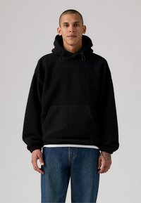 Sort fleece hoodie med dråbesnore og frontlomme, med et struktureret, blødt stof. Kombineret med blå lige ben jeans.