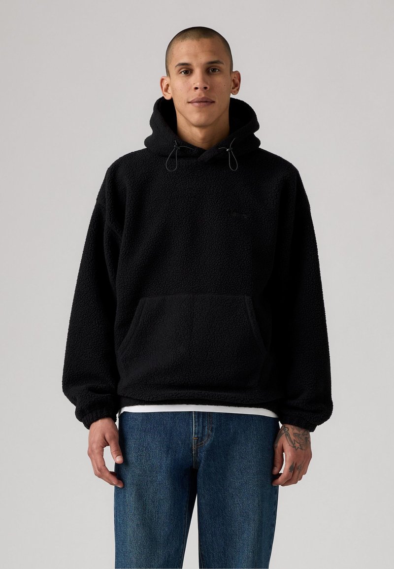 Sort fleece hoodie med dråbesnore og frontlomme, med et struktureret, blødt stof. Kombineret med blå lige ben jeans.