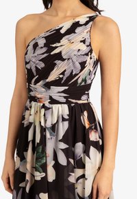 Robe noire à fleurs à une épaule avec un corsage plissé et une taille froncée, ornée de grandes fleurs blanches et pastel.