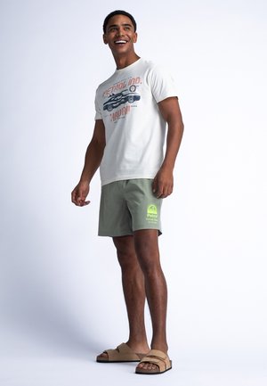 Lichtgrijs T-shirt met autografiek; olijfgroene shorts met een logo; tan instappers; korte mouwen; losse pasvorm.