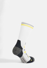 Calza sportiva bianca con strisce grigie e gialle, tallone rinforzato grigio e punta nera. Materiali testurizzati migliorano aderenza e supporto.