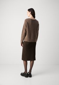 Pull en maille marron avec une coupe décontractée, associé à une jupe côtelée sombre et des chaussures noires imposantes. Des tons neutres et des lignes simples caractérisent l'ensemble.