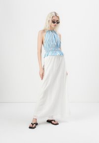 Top holgado azul y blanco a rayas con cintura peplum fruncida, combinado con una larga falda maxi de encaje blanca y chanclas negras.