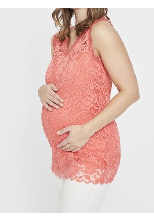 Coral lace maternity top with a v-neck and floral patterns, featuring a scalloped hem and fitted design, worn over white pants.
