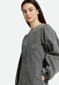 Vestido de denim gris de corte oversize con mangas largas abullonadas, cuello redondo y detalles de costura visibles. La tela tiene un aspecto suave y texturizado.