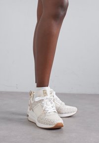 Scarpe da ginnastica bianche con una tomaia testurizzata caratterizzata da un motivo logo beige chiaro, design con lacci e una suola in gomma con un accento color tan.