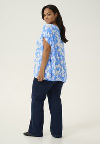 Light blue floral blouse with white patterns, short sleeves, flowing design, paired with dark blue flared jeans and black shoes.