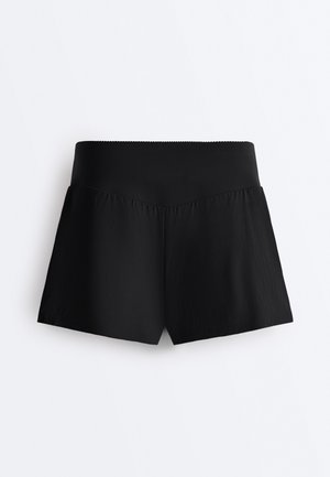 Černé krátké kalhoty s vysokým pasem, širokým pasem a mírným V-švem vpředu, zobrazené na bílém pozadí.