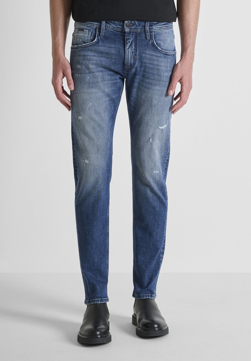 Muške plave traperice s uskim krojem, izblijedjelim finišom, suptilnim trošenjem, dizajnom s pet džepova i patentnim zatvaračem s gumbom.