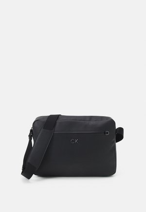 Borsa a tracolla nera con finitura in tessuto liscio, dotata di una tasca con zip frontale e una tracolla regolabile. Logo impresso sulla parte anteriore.