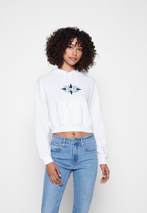 White cropped hoodie with a front pocket, drawstring hood, and a multi-colored graphic design at the center. Paired with light blue jeans.