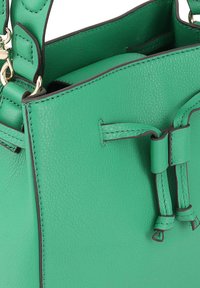 Groene leren handtas met textuurafwerking, contrasterende zwarte stiksels en handvatten aan de bovenkant. Voorzien van een unieke knoopsluiting.