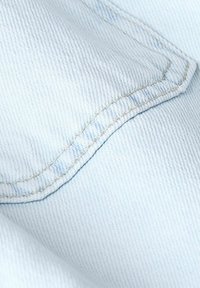 Lichtblau denim stof met een gestructureerd oppervlak, met een zichtbare naad gestikt met contrasterend gele draad.