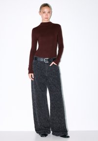 Bordo dug dugi rukav majica u kombinaciji s crnim širokima hlačama od teksturirane tkanine, koje imaju crni remen i prednje džepove. Glatka tkanina i opušteni kroj.