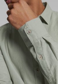 Langsleeve, lichtgroen knoopshirt met een zachte textuur, voorzien van een puntige kraag, knopen op de manchetten en geplooide details op de mouwen.