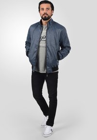 Denim bomberjakke med en grå hettegenser under, svarte jeans og hvite sneakers. Har glidelås og ribbede ermer.