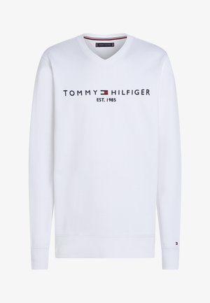 Sweat-shirt blanc à manches longues avec col en V, portant le texte "Tommy Hilfiger EST. 1985" et le logo drapeau sur la poitrine, ainsi qu'un petit logo sur le poignet gauche.