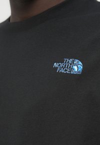 Μαύρο βαμβακερό μπλουζάκι με μικρό μπλε κεντημένο λογότυπο "The North Face" στο αριστερό στήθος. Λαιμόκοψη στρογγυλή, κοντά μανίκια.