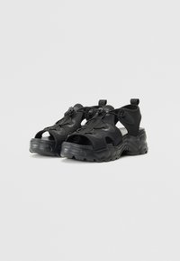 Black open-toe sandals feature a chunky sole, adjustable straps, and a textured finish, designed for comfort and stability.