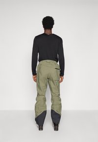 Pantaloni de exterior verde măsliniu cu accente negre, având un croi lejer, fermoare pe părțile laterale și tivuri inferioare întărite.