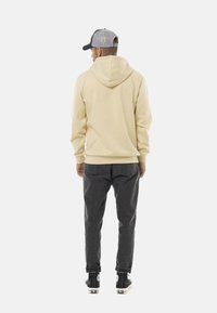 Sweatshirt beige à capuche avec une coupe décontractée, associé à un pantalon gris foncé et des baskets montantes noires. Détails de couture visibles.