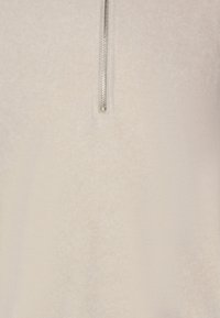 Fleece pullover in lichtbeige met een halve rits. Zachte textuur, subtiel patroon en een ontspannen pasvorm voor comfort en warmte.