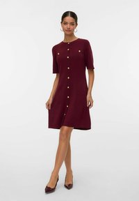 Abito bordeaux fino al ginocchio con maniche corte, con dettagli in bottoni dorati e una vestibilità dritta. Tessuto a maglia morbido, scollatura rotonda e tasche laterali.