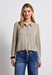 Ljusbeige långärmad topp med krage, knappstängning och dragsko i nederkant. Bärs med blåjeans. Slät textur.