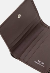 Portafoglio in vera pelle marrone della Guess aperto per mostrare gli scomparti per carte e la chiusura a bottone su uno sfondo bianco.