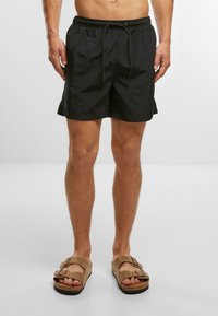 Zwarte zwembroek van lichtgewicht stof, met een elastische tailleband en een trekkoord. Perfect te combineren met bruine open teensandalen.