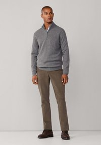 Pullover grigio in maglia con colletto con zip, abbinato a pantaloni marrone chiaro e scarpe marrone scuro. Tessuto morbido e design aderente.