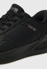 Juodos Skechers sportbačiai su tekstūruotu, lygios odos viršumi, su auksinėmis ženklinimo detalėmis šone ir paminkštintu apvadu komfortui.